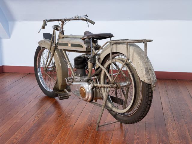 Motocyclette TRIUMPH 1916 de couleur kaki moteur monocylindre 4 temps 550cm3 (85x97) soupapes latérales allumage par magnéto transmission primaire par chaîne boîte STURMEY-ARCHER 2 vitesses à main droite transmission secondaire par courroie suspension avant par fourche pendulaire pas de suspension arrière vitesse 80km/h