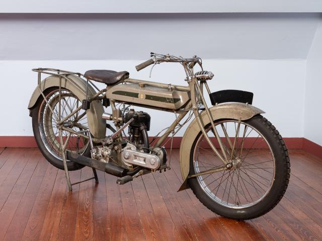 Motocyclette TRIUMPH 1916 de couleur kaki moteur monocylindre 4 temps 550cm3 (85x97) soupapes latérales allumage par magnéto transmission primaire par chaîne boîte STURMEY-ARCHER 2 vitesses à main droite transmission secondaire par courroie suspension avant par fourche pendulaire pas de suspension arrière vitesse 80km/h